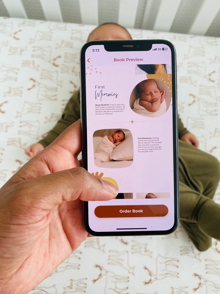 A hand holding a phone showing the Dujourbaby Book Preview screen with a baby photo and an Order Book button