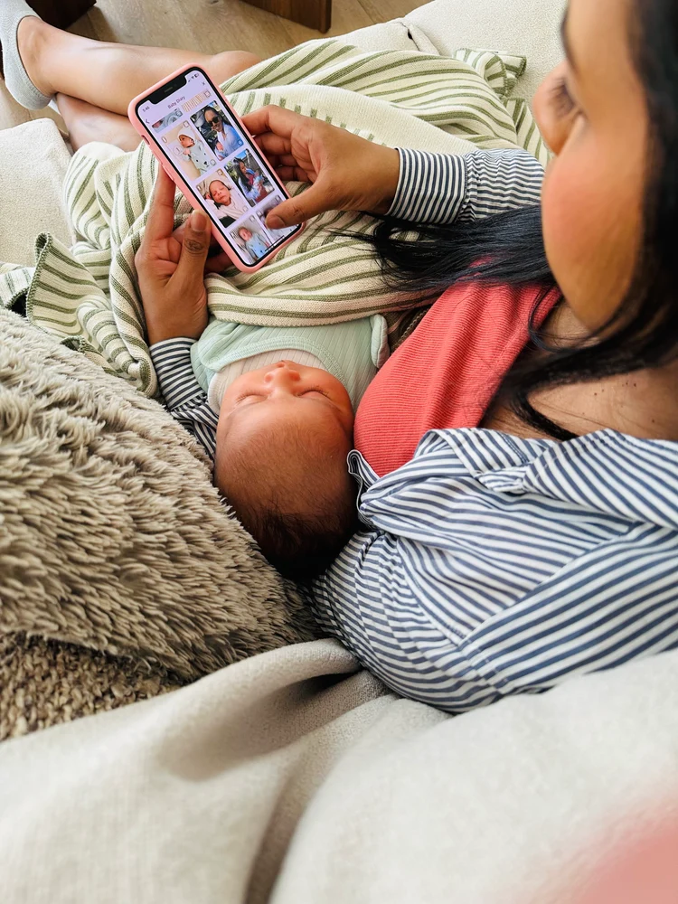 A mother relaxing on the couch with her baby while using the Dujourbaby app on her phone